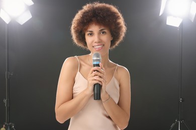 Photo of Curly young woman with microphone singing on black background