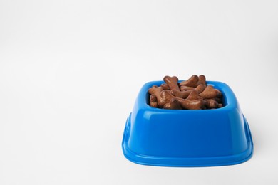 Blue bowl with bone shaped dog cookies on white background, space for text