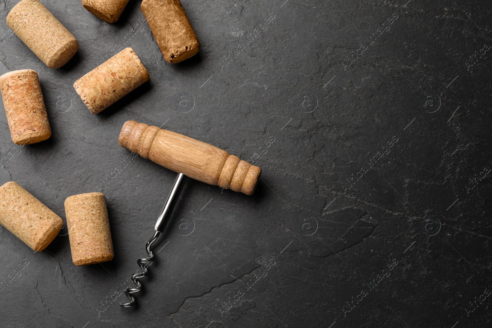 Photo of Corkscrew and wine bottle stoppers on slate table, flat lay. Space for text