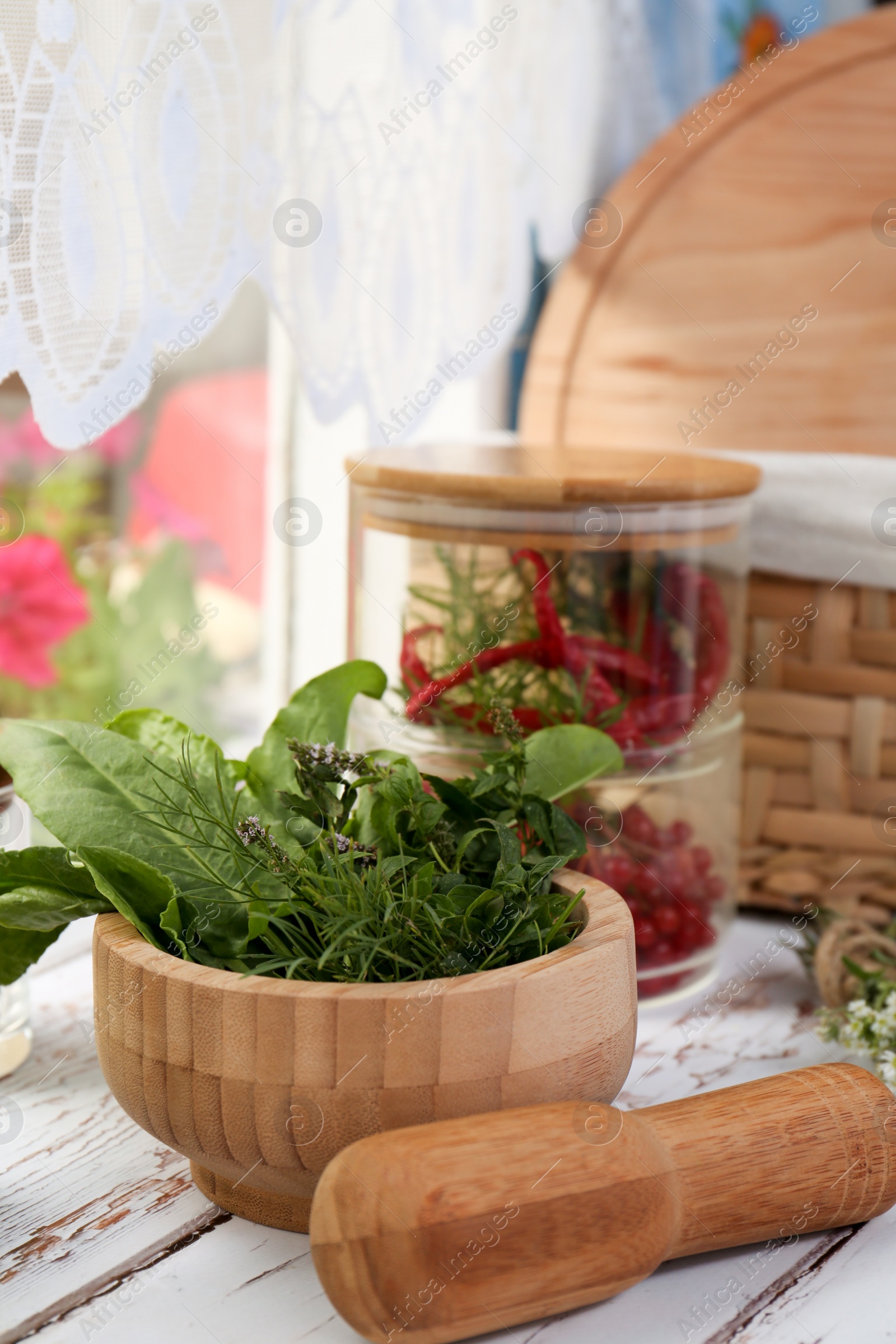 Photo of Mortar with pestle and fresh green herbs on white wooden table near window. Space for text