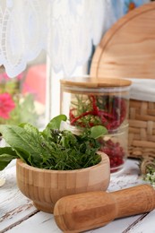 Photo of Mortar with pestle and fresh green herbs on white wooden table near window. Space for text