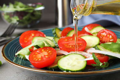 Photo of Adding cooking oil to delicious salad on table, closeup