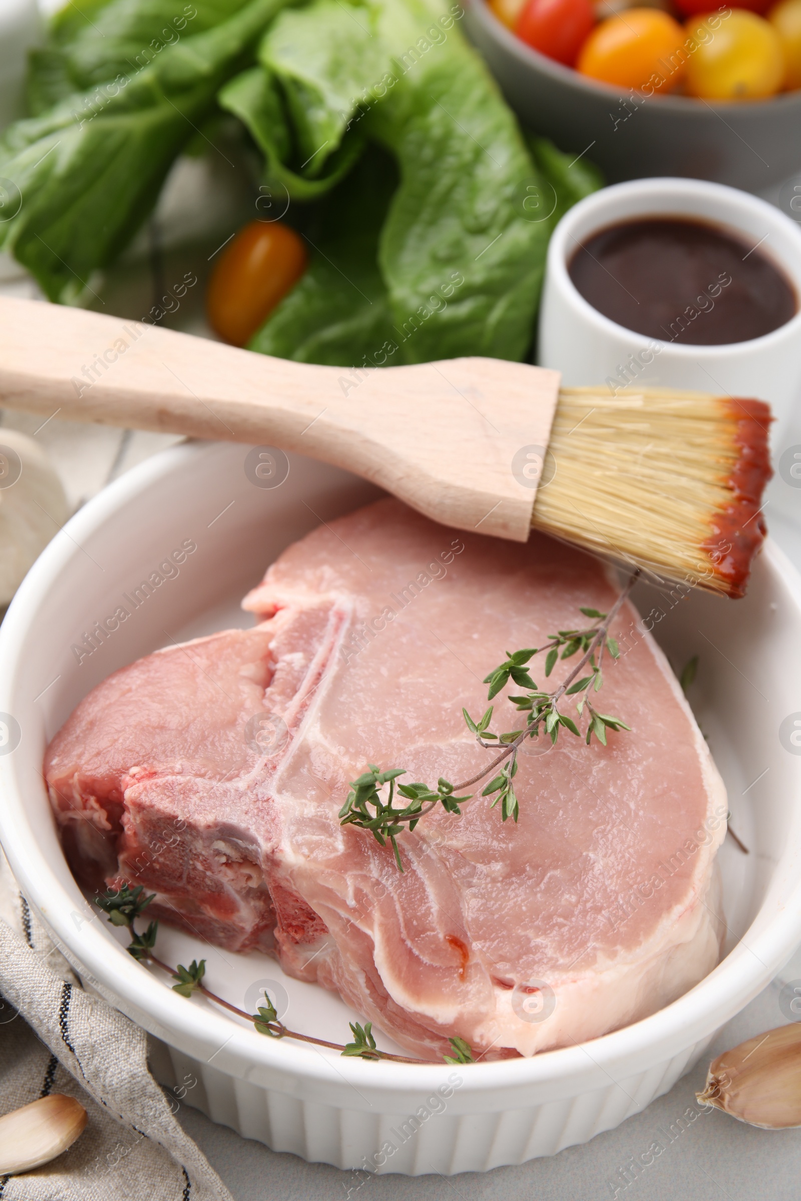 Photo of Raw meat, thyme and brush with marinade on light table, closeup