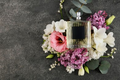 Photo of Bottle of luxury perfume and floral decor on dark grey table, top view. Space for text