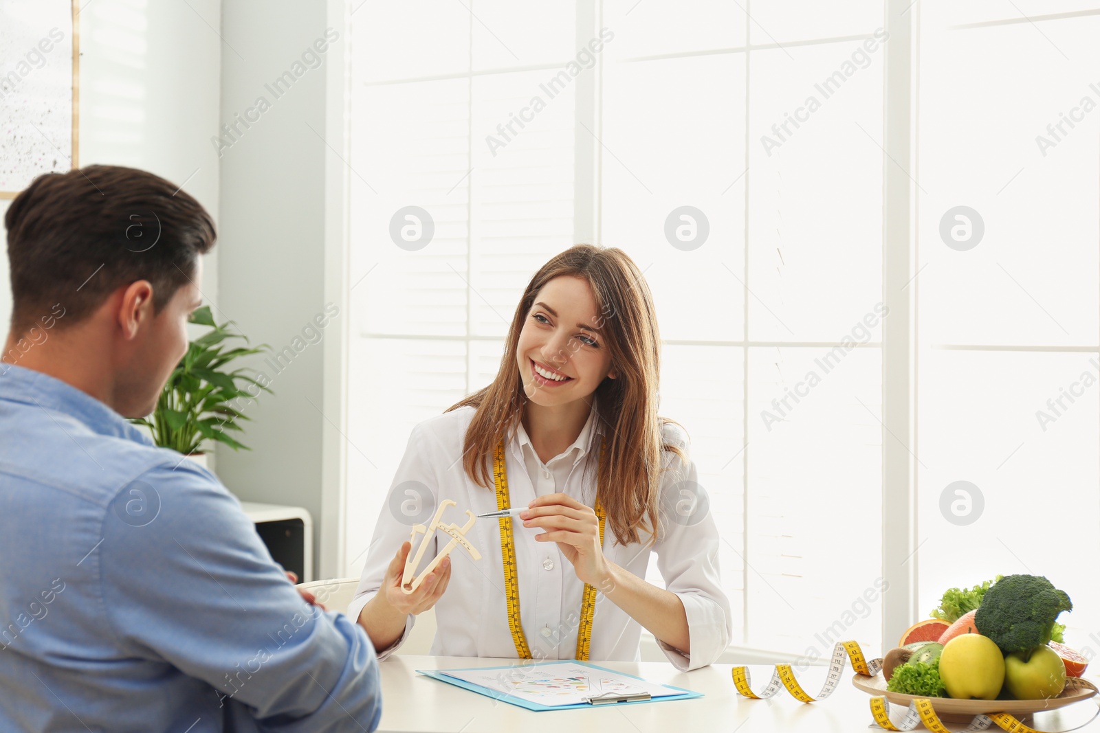 Photo of Young nutritionist consulting patient at table in clinic