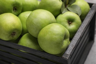 Photo of Fresh green apples in black crate on table, closeup