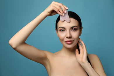 Photo of Beautiful young woman doing facial massage with gua sha tool on blue background