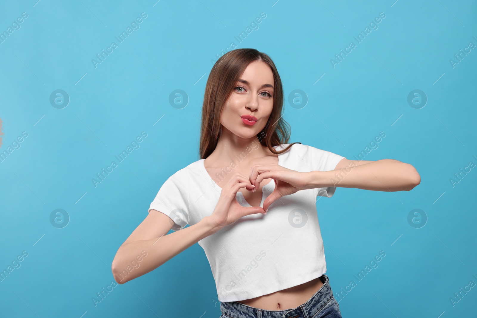 Photo of Beautiful young woman blowing kiss and making heart with hands on light blue background