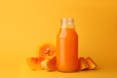 Photo of Tasty pumpkin juice in glass bottle and cut pumpkin on orange background