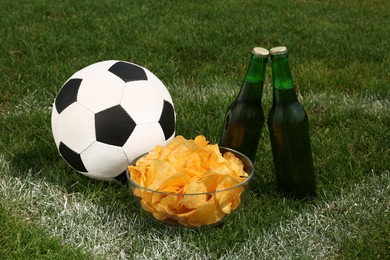 Photo of Football ball with beer and chips on green field grass