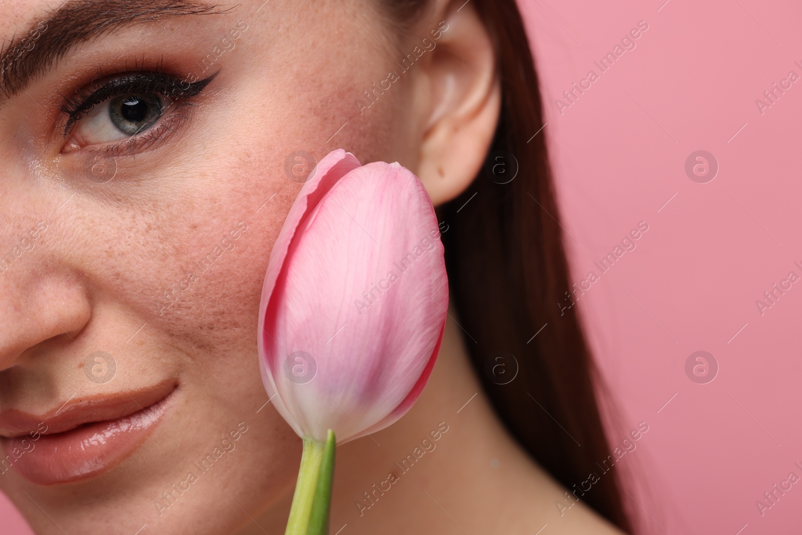 Photo of Beautiful woman with freckles and tulip on pink background, closeup