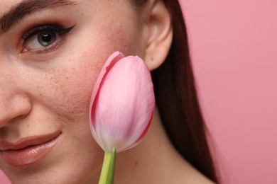 Beautiful woman with freckles and tulip on pink background, closeup