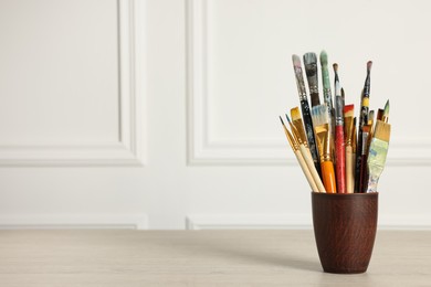 Photo of Different paintbrushes in holder on white wooden table. Space for text