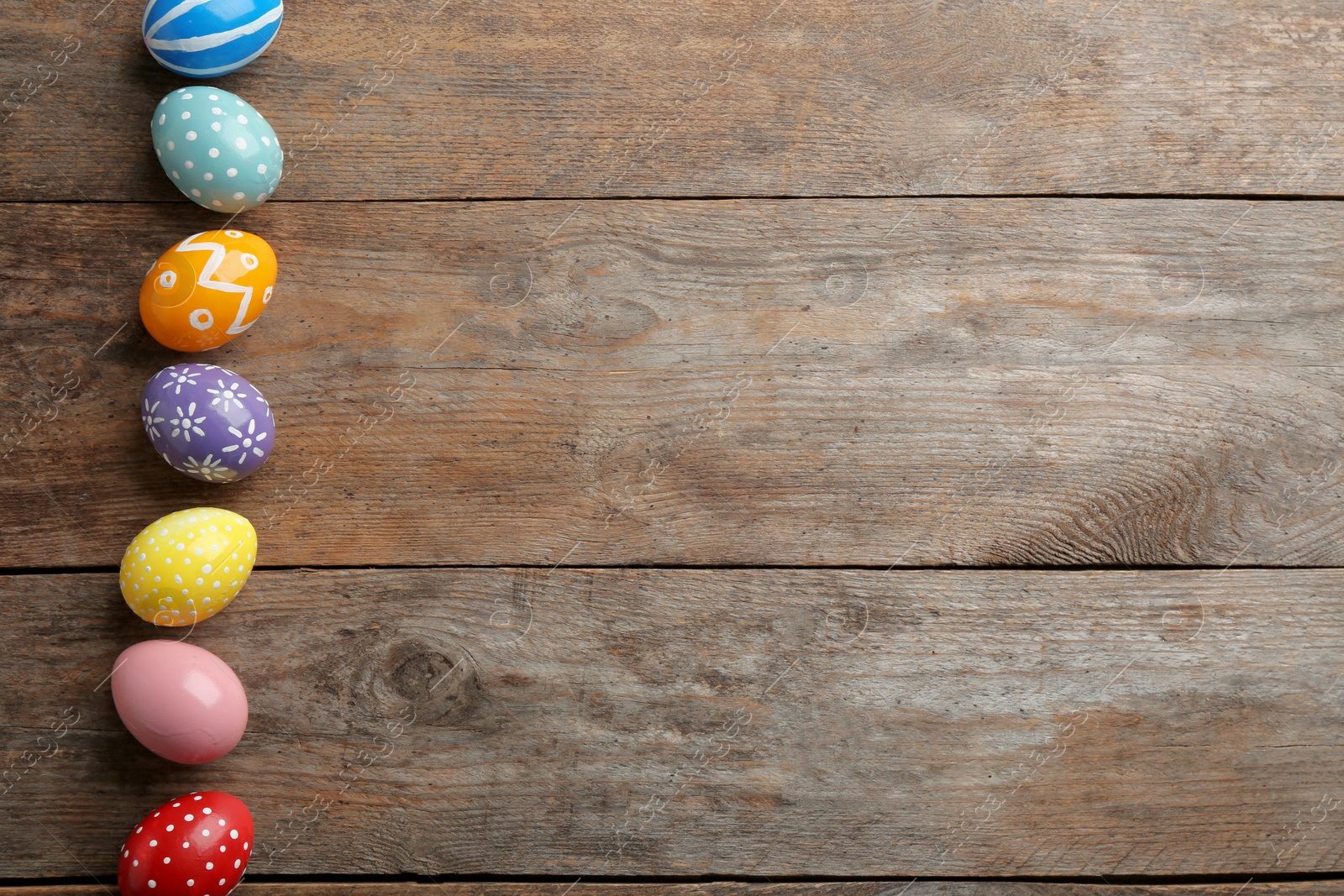 Photo of Flat lay composition of painted Easter eggs on wooden table, space for text