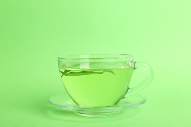 Photo of Cup of aromatic green tea with leaves on color background