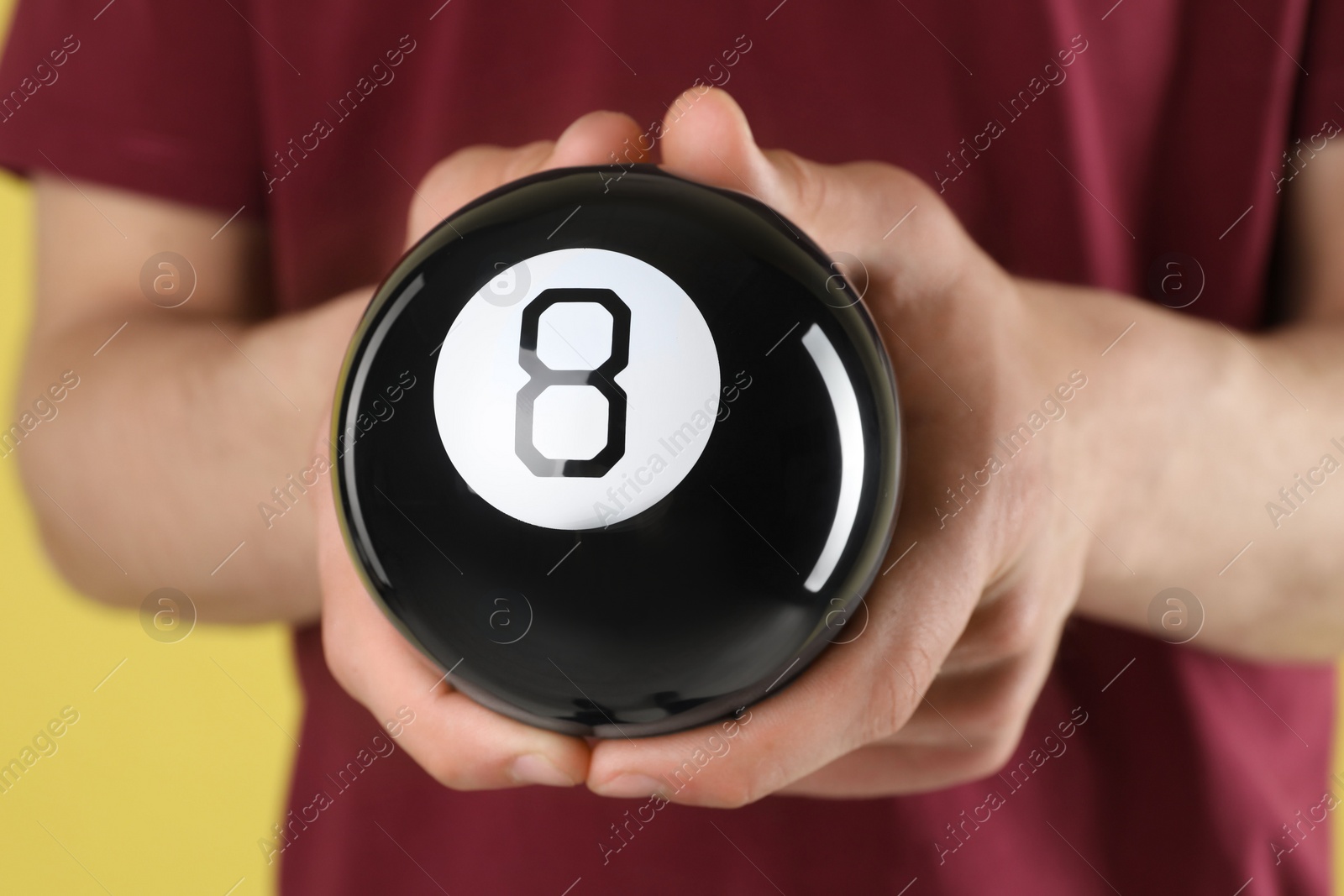 Photo of Man holding magic eight ball on yellow background, closeup