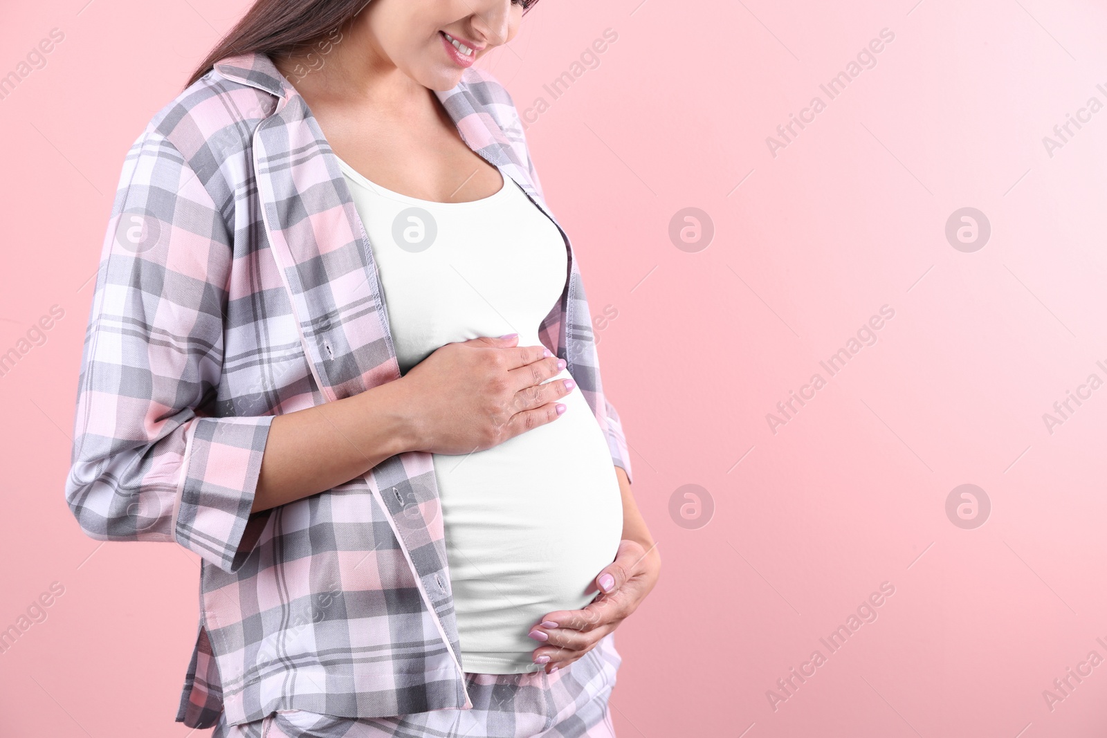 Photo of Young pregnant woman holding hands on belly against color background, closeup. Space for text