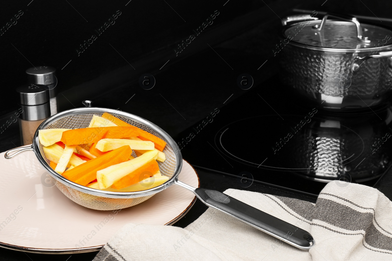 Photo of Sieve with cut raw parsnips and carrots on black table in kitchen