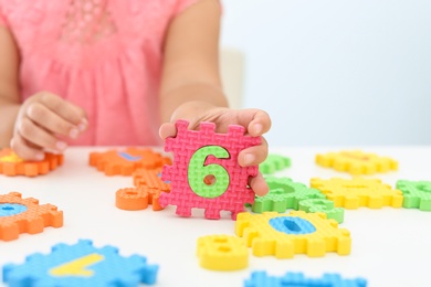 Photo of Little girl playing with colorful puzzles at white table, closeup. Educational toy