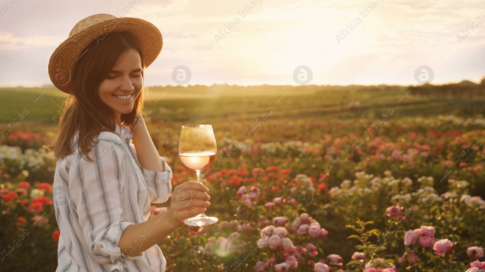 Photo of Woman with glass of wine in rose garden on sunny day. Space for text