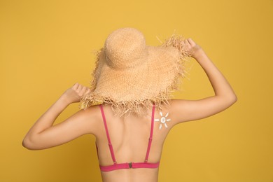 Photo of Teenage girl with sun protection cream on her back against yellow background
