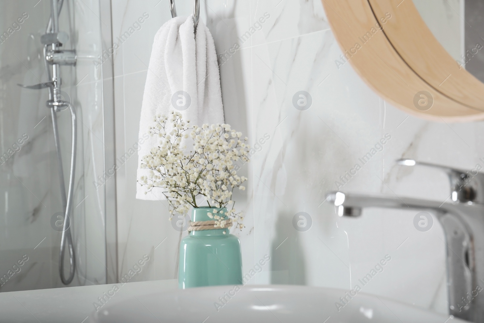Photo of Vase with flowers and soft towel in bathroom interior