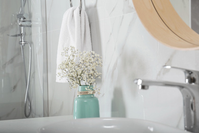 Photo of Vase with flowers and soft towel in bathroom interior