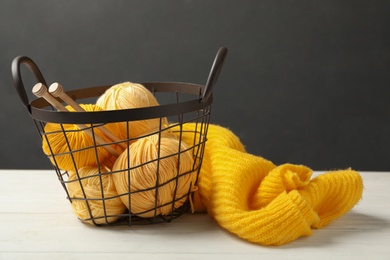 Soft yellow woolen yarns with knitting needles and sweater on white table