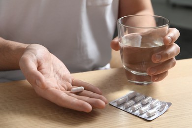 Photo of Man with glass of water and pill at wooden table, closeup