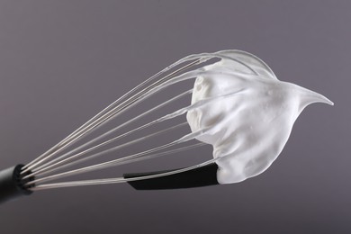 Photo of Whisk with whipped cream on grey background, closeup