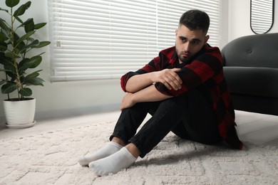 Sad man sitting on floor at home. Space for text