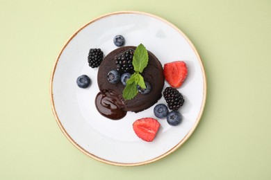 Plate with delicious chocolate fondant, berries and mint on light green table, top view