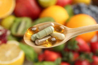 Photo of Different vitamin pills in spoon over fresh fruits, closeup