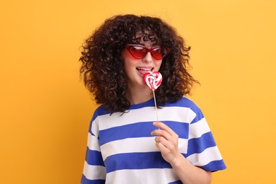 Beautiful woman in sunglasses with lollipop on yellow background