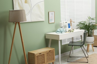 Photo of Modern sewing machine with cloth and craft accessories on white table near window in room