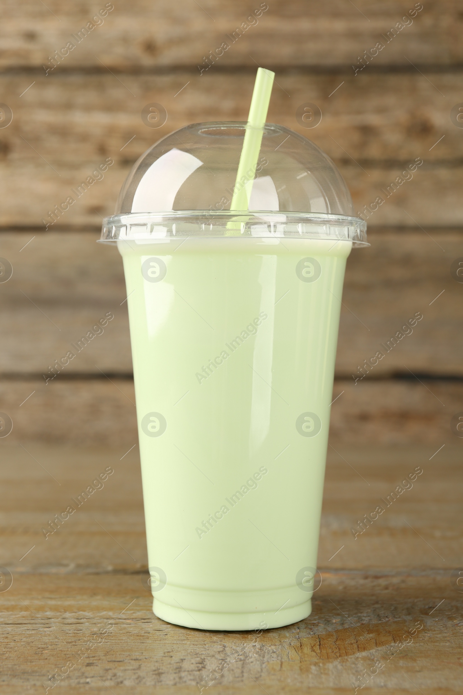 Photo of Plastic cup of tasty smoothie on wooden table