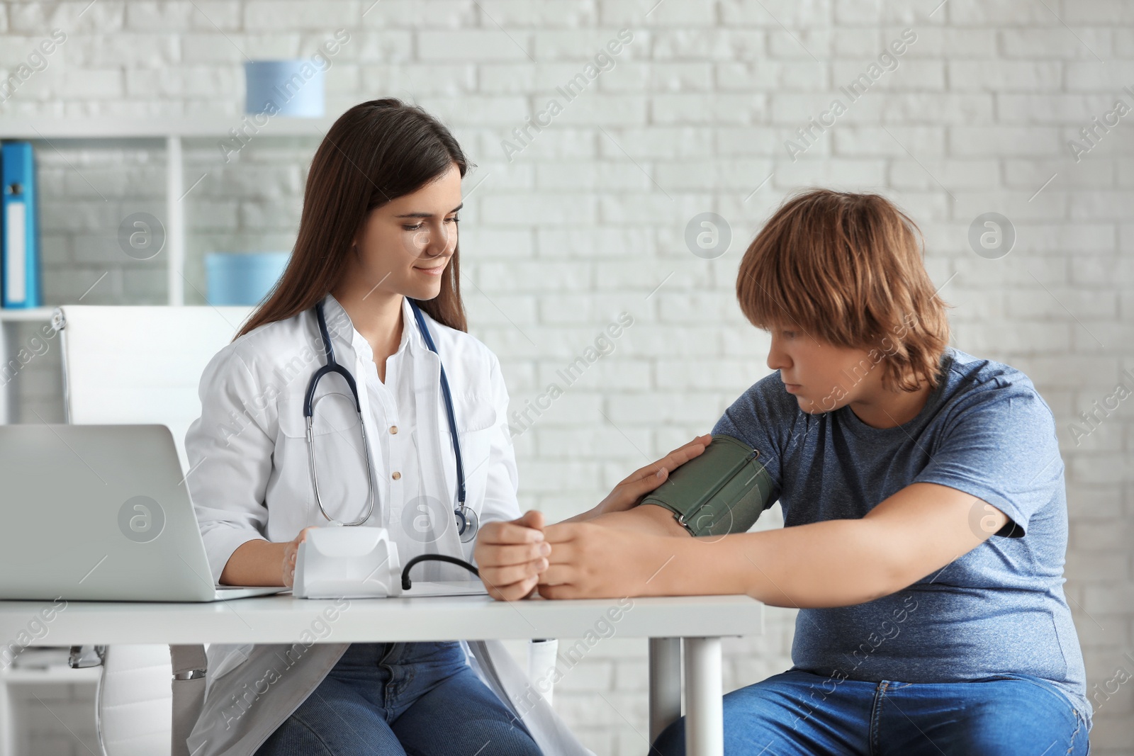 Photo of Female doctor checking overweight boy's blood pressure in clinic