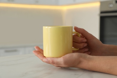 Woman with yellow cup at table indoors, closeup