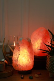 Himalayan salt lamps, candle, houseplant and gemstones on wooden table near white wall indoors
