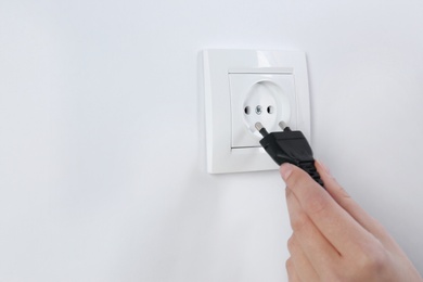 Woman putting plug into power socket on white background, closeup. Electrician's equipment