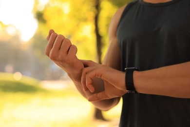 Photo of Man checking pulse after training on sunny day, closeup