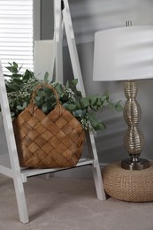 Photo of Stylish straw bag with beautiful bouquet and lamp indoors