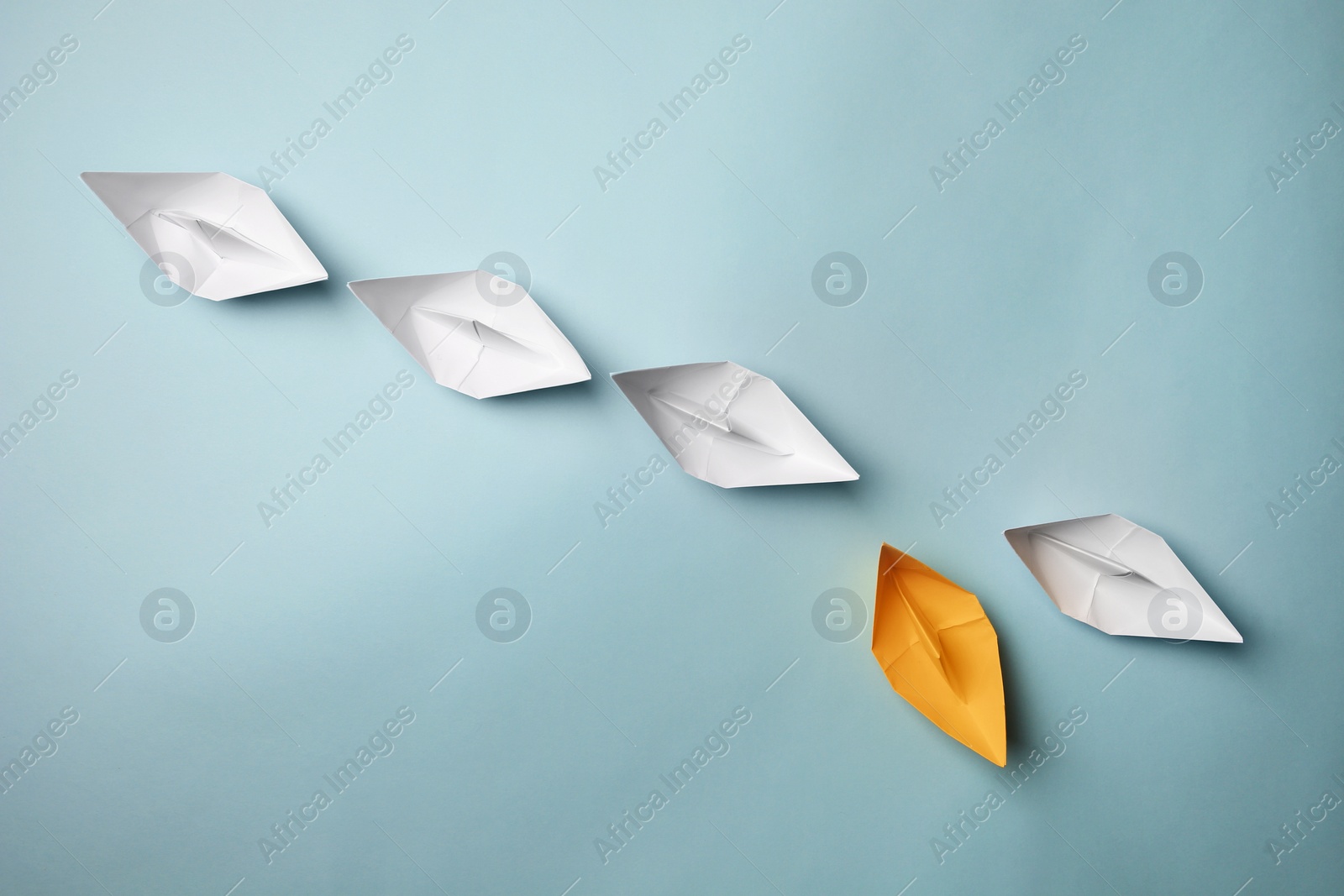 Photo of Yellow paper boat floating away from others on light background, flat lay with space for text. Uniqueness concept