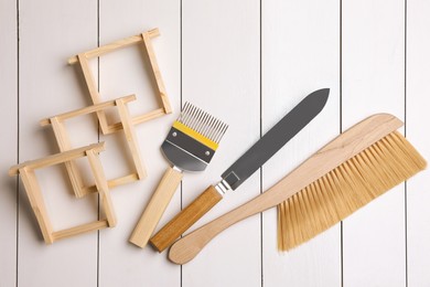 Photo of Honeycomb frames and beekeeping tools on white wooden table, flat lay