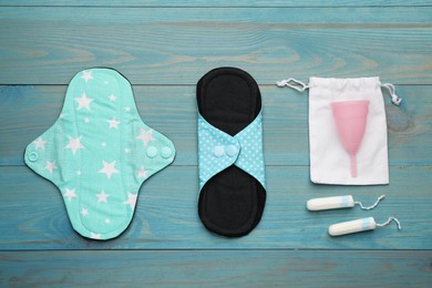 Photo of Reusable cloth pads, menstrual cup and disposable tampons on light blue wooden table, flat lay