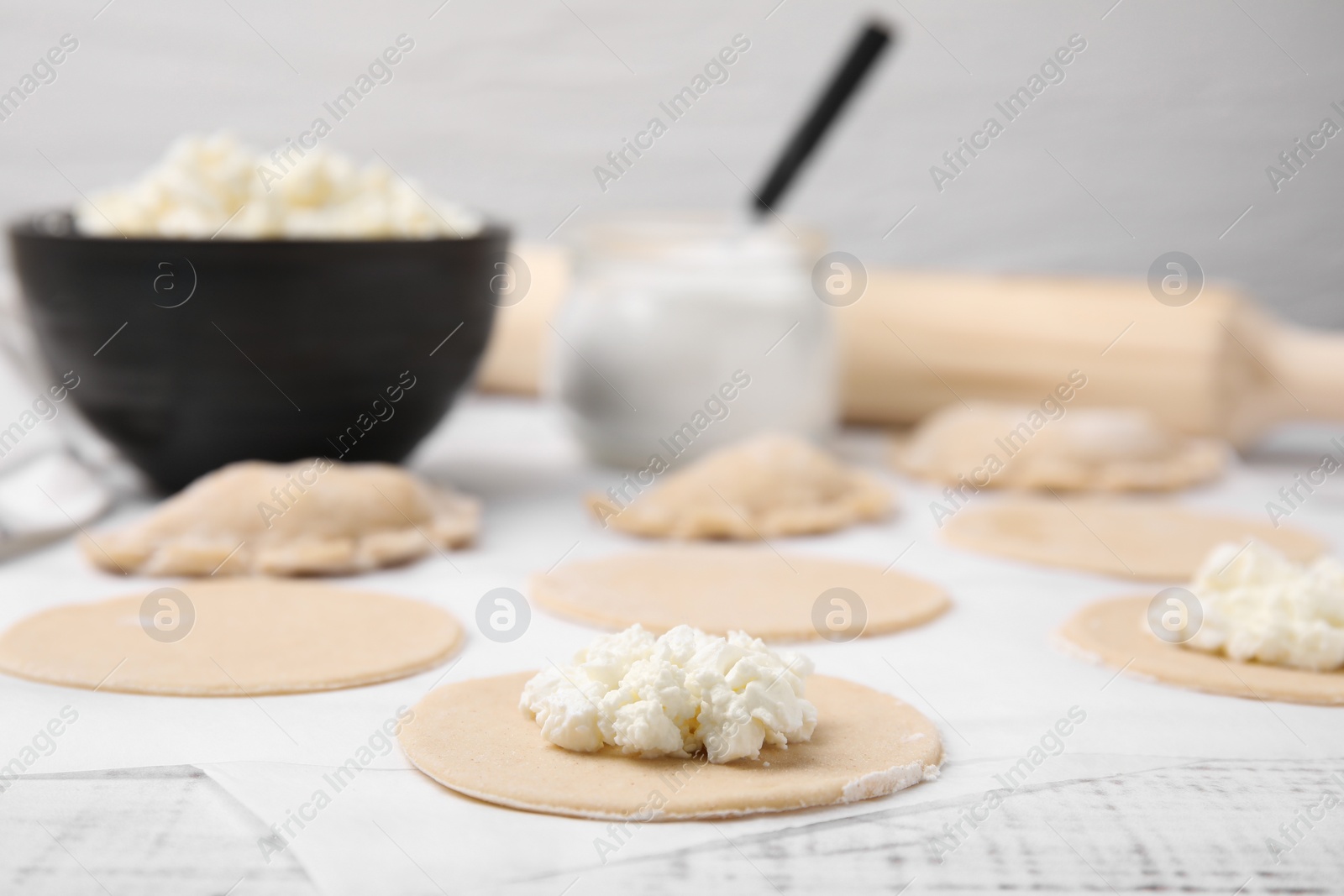 Photo of Process of making dumplings (varenyky) with cottage cheese. Raw dough and ingredients on white table, closeup