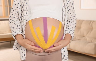 Pregnant woman with kinesio tapes on her belly at home, closeup