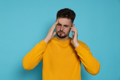 Stressed man in yellow sweatshirt talking on phone against light blue background