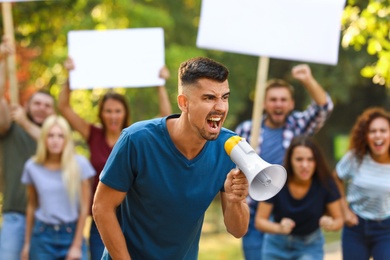 Angry young man with megaphone at protest outdoors