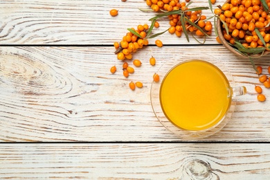 Photo of Sea buckthorn tea and fresh berries on white wooden table, flat lay. Space for text